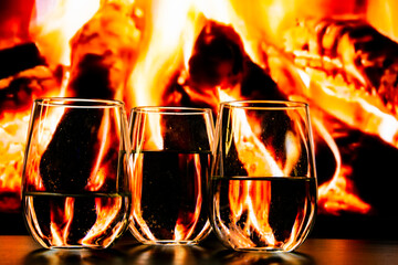 A beautiful glass with a drink near the fireplace. Firewood and fire. Glass and liquid.