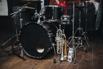 A black drum kit and a microphone stand are on stage and next to them are two trumpets (alto and bass) and a white tambourine. The concept of a live concert of a jazz band.