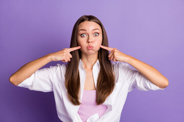 Photo of childish young girl puffed cheeks direct fingers face wear white shirt isolated violet...