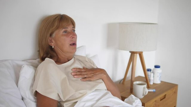 Middle aged Caucasian woman chesty coughing while lying in her sickbed