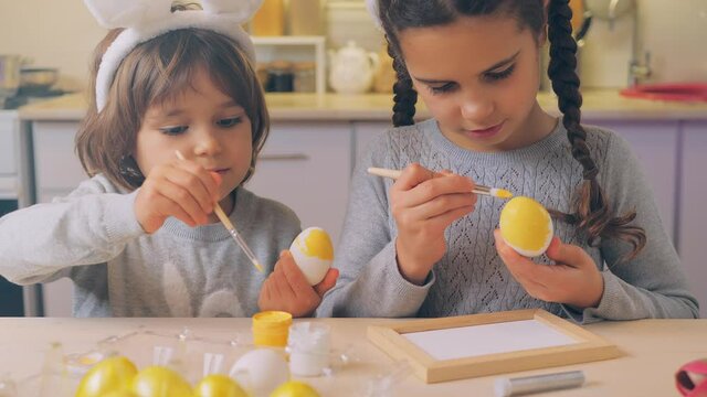Happy Easter Holiday. Beautiful children paint and decorate an egg for a traditional spring dinner at home. Little girl and boy playing, fooling, drawing easter eggs