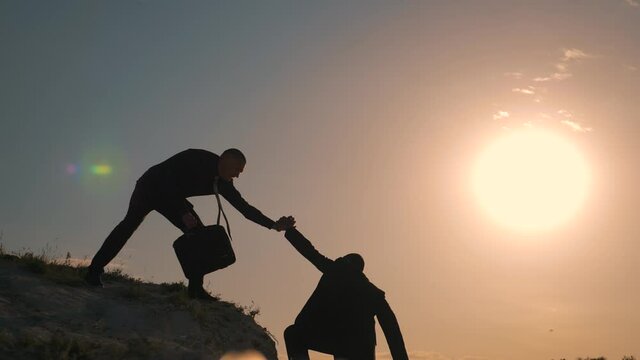 Two businessmen climb to top of mountain. Helping hand in business. Teamwork in business. Businessmen help to overcome difficulties. Helping hand in teamwork. Business partnership business success