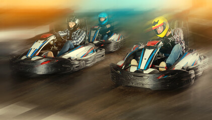 Group of happy male and females in helmets driving racing cars at kart track © JackF