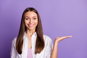 Photo of cheerful young girl palm hold empty space beaming smile wear white shirt isolated violet color background