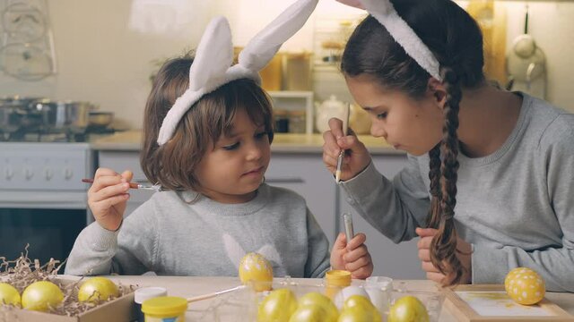 Happy Easter Holiday. Beautiful children paint and decorate an egg for a traditional spring dinner at home. Little girls playing, fooling, drawing easter eggs