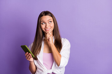 Photo of minded girl hold telephone look up empty space finger chin wear white shirt isolated violet color background