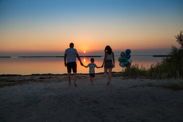 Family: dad, mom and child hold hands against the backdrop of the sea sunset.