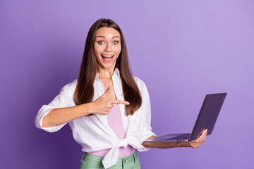 Photo portrait of girl pointing finger at laptop in hand isolated on vivid purple colored background