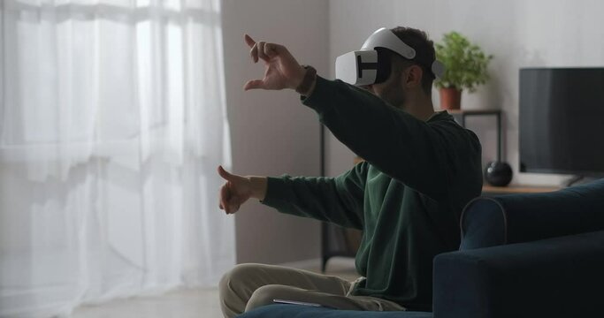 man is sitting at home and using virtual reality goggles, gesticulating by hands, swiping and zooming pictures
