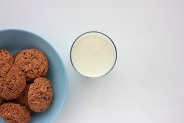Oatmeal cookies and glass of milk on white table. Overhead view of oat biscuits in blue bowl on white background with copy space. Healthy snack