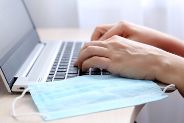 Female hands on laptop keyboard and removing medical mask on a desk. Woman types on the laptop...