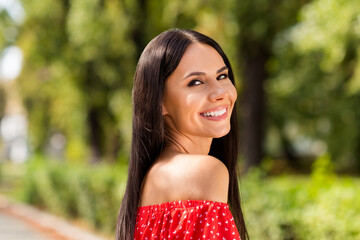 Side profile photo portrait of cheerful woman smiling wearing stylish red dress with off-shoulders laughing on green streets