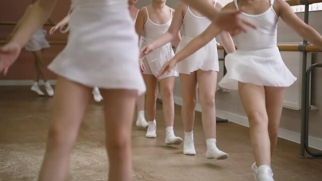 Small children are doing ballet. Girls in white dresses and pointe shoes run in circle