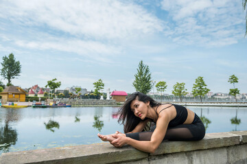 Fototapeta na wymiar Beautiful fitness trainer doing yoga exercises on stretching and flexibility near lake