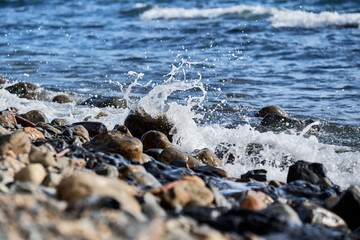 Sea waves break on shingle beach. Small wave rolls onto shore and splash of foam flies in different directions. Beautiful marine minimalist screensaver.