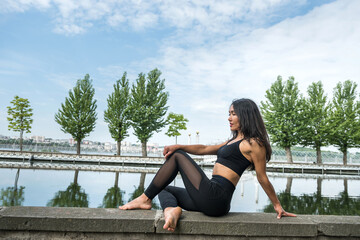 Pretty slim woman  wearing sportive clothes,  sitting by the lake and relaxing after  exercise after hard workday