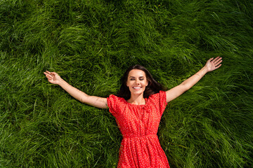 Naklejka na ściany i meble Photo of funny cute young woman dressed red off-shoulders dress relaxing green grass arms sides outdoors backyard