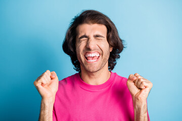 Photo of positive happy brunet hair arabic man close eyes scream hold fists wear pink t-shirt isolated over blue color background