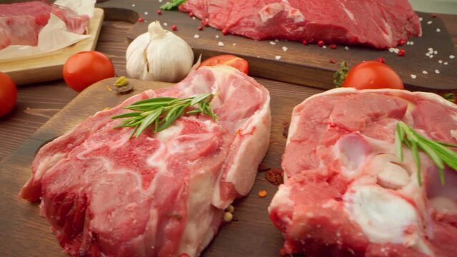 Fresh raw meat steaks on wooden board with spices close up