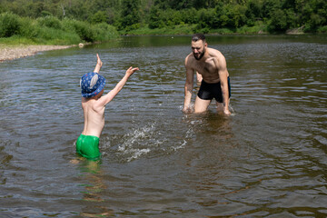 Happy child and father playing, splashing water in river. Family vacation concept