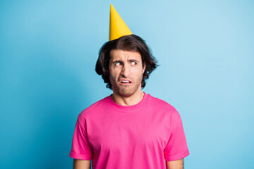 Portrait of nervous irritated guy wearing yellow celebratory cap looking aside dislike copy space...