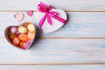 Candies in white heart shaped gift box on wooden background in copy space