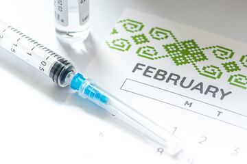 Syringe, vial and calendar with month of February on a white table ready to be used. Covid or Coronavirus vaccine background
