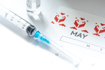 Syringe, vial or phial and calendar with month of May on a white table ready to be used. Covid or Coronavirus vaccine background