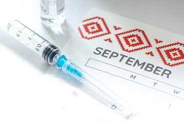 Syringe, vial and calendar with month of September on a white table ready to be used. Covid or...