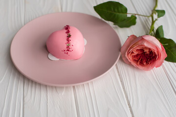 Heart-shaped pink cake with mirror glaze on a pink plate next to a bouquet of pink and white roses on a white wooden background. Congratulations on Valentine's Day, Happy Birthday, Women's Day.
