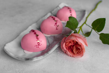 Selective focus heart-shaped pink cakes with mirror glaze decorated with gold leaf with rose on a gray stone plate. Greeting card on on Valentine's Day, Happy Birthday, Women's Day.