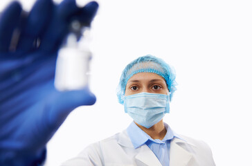 Female doctor in protective workwear looking at the vaccine in her hand while showing it to the camera. Isolated on white background.