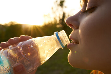 woman drinks water from a plastic bottle in summer outdoors