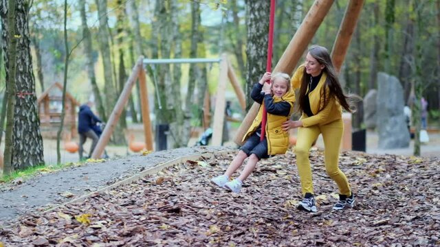 Little girl having fun outdoors. Zipline for kids. Slow motion footage. mom or nanny plays with her daughter on the playground. happy childhood concept.