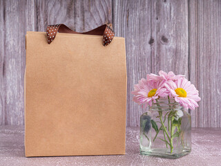 Brown paper bag packaging with ribbon handles placed on a gray stone background with a wooden wall. Side view with copy space for text