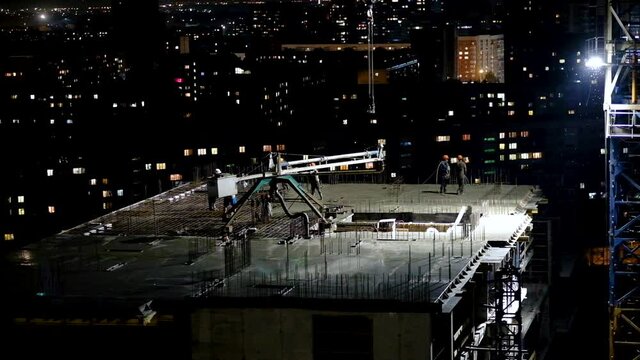 Construction workers pouring wet concrete using concrete spider hose or pump work at high-rise site in night