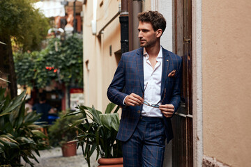 Young handsome man in classik checked suit standing on the street and holding sunglasses