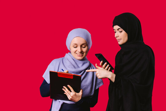 Young Muslim businesswoman in hijab with documents and a smartphone on a red studio background with a smile decide business matters.