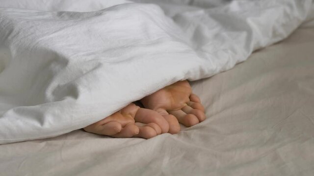 Sleepy person covered with white soft blanket wriggles toes awakening in comfortable bed in sunny morning extreme close view