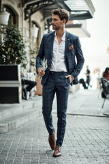 Handsome male model in checked suit walking on the street with newspaper - 411774563