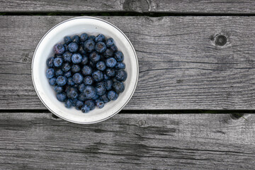 Fresh ripe blueberries in a white bowl on the rough wooden boards