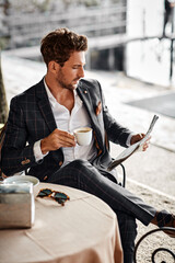 Handsome man drinking coffee and reading newspaper in cafe