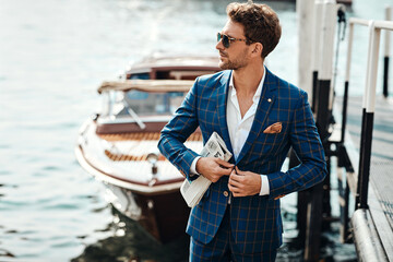 Young handsome man in classic suit over the blurred lake buttoning his jacket - 411775586