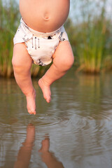 A baby wearing a cloth reusable diaper with the baby's toes dipped in a river.