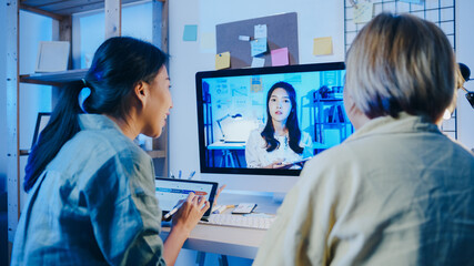 Asia businesswomen using desktop talk to colleagues about plan in video call meeting at living room. Working from house overload at night, remotely work, social distancing, quarantine for coronavirus.