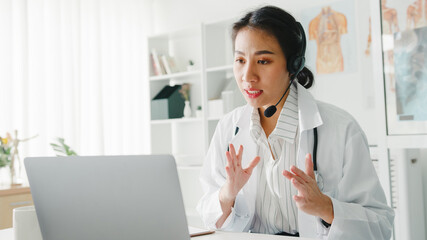 Young Asia lady doctor in white medical uniform with stethoscope using computer laptop talking...