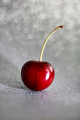 Closeup one red cherry fruit with root on light grey background with bokeh