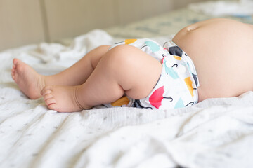 A baby lying on a bed with the focus on the baby's legs and cloth diaper with a pretty umbrella...