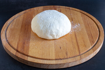 Raw dough for pizza on wooden board on black background