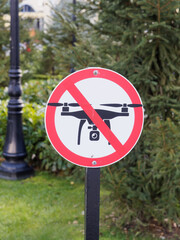 A round sign with a quadcopter on a white background crossed out by a red line against the background of green vegetation